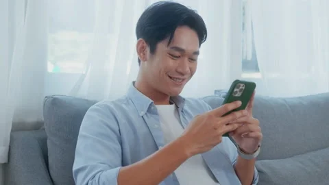 Young asian man using  smart phone  on sofa in living room Stock Footage 212892095