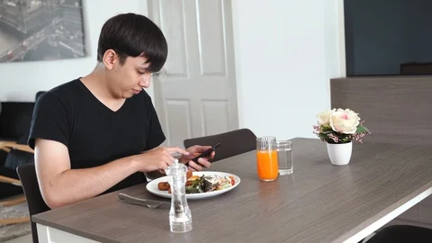 Young asian man using smartphone and eating breakfast in the apartment Stock Footage 107742255