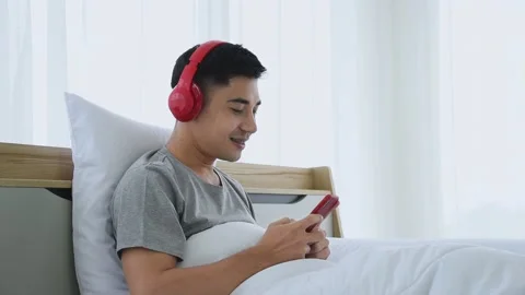 Young Asian man using a smartphone to listening to music in bedroom. Stock Footage 144087391