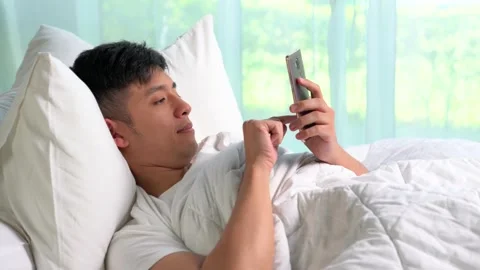 Young Asian man using a smartphone in his bed Stock Footage 156639017