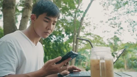 Young asian man using smartphone doing online transactions with laptop computer Stock Footage 270320851