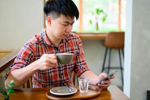Young asian man using smartphone and having coffee Stock Photos