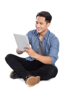 Young asian man using tablet pc while sitting on the floor, isol Stock Photos