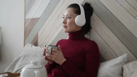 Young asian multi ethnic dreamy woman in headphones holding cup enjoy favourite Stock Footage 169810575
