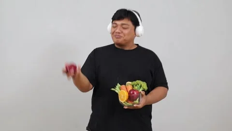 Young Asian obese man dancing, listening to music in headphones while holding Stock Footage 342475388