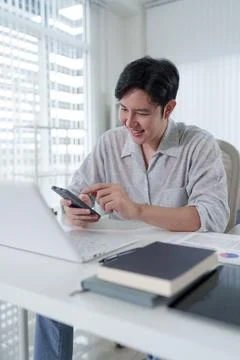 Young Asian professional smiling while using smartphone at modern office de.. Stock Photos