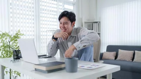 Young Asian professional smiling while working from home with laptop in bri.. Stock Photos
