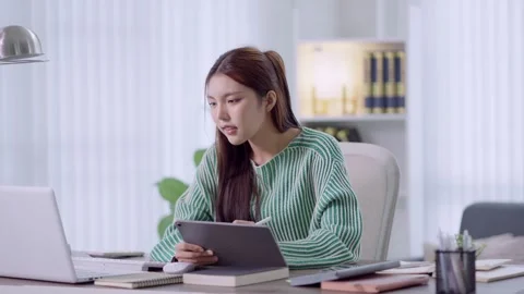 Young Asian professional using tablet and laptop for remote work at bright .. Stock Footage 342533135
