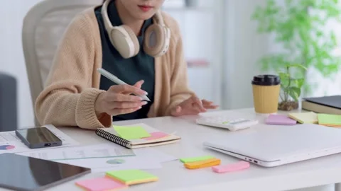 Young Asian professional writing notes on sticky pad during remote work ses.. Stock Footage 337367296