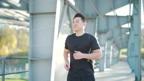 Young asian runner running on modern urban stadium background. Morning jog sport Stock Footage 165617459