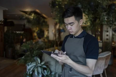 Young Asian server using digital tablet in restaurant Stock Photos