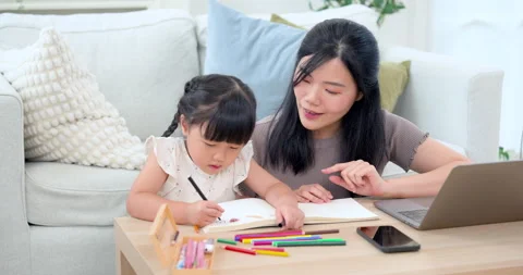 Young Asian single mother points toward workbook while little daughter sketches Video stock 334764057