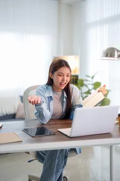 Young Asian student gesturing while reading notebook during online educatio.. Stock Photos