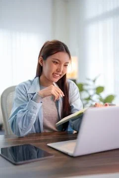 Young Asian student smiling while studying with laptop and notebook at wood.. Stock Photos