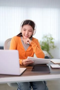 Young Asian student smiling while studying with headphones and notebook dur.. Stock Photos