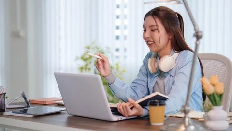 Young Asian student using laptop and notebook for e-learning at bright home.. Fotos de archivo