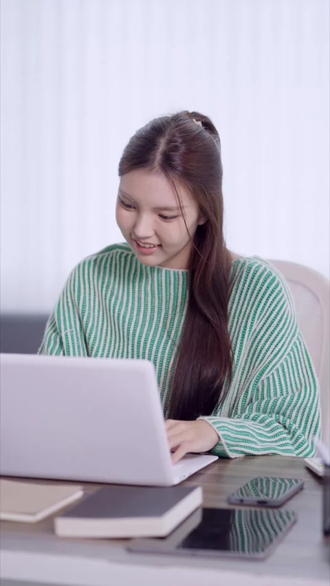 Young Asian student working on laptop computer at home desk with books and .. Stock Footage 342533168