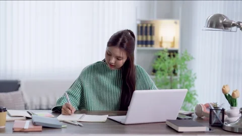Young Asian student writing notes in notebook while studying with laptop at.. Stock Footage 341682803