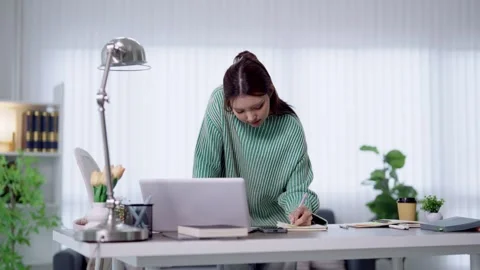 Young Asian student writing notes while studying with laptop at bright home.. Stock Footage 341682818