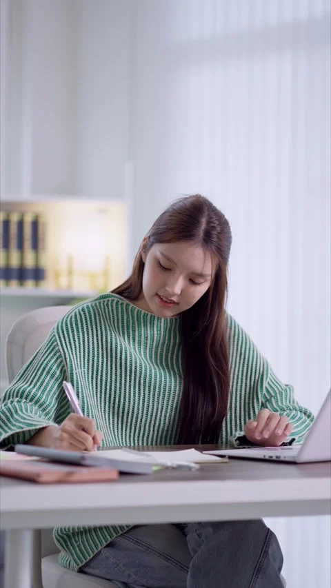 Young Asian student writing notes while using laptop for online learning in.. Stock Footage 342533301