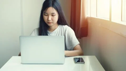Young asian teen millennial woman using computer laptop with smart phone on d Stock Photos
