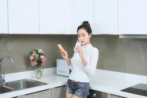 Young Asian using phone while drinking milk in kitchen. Foto stock