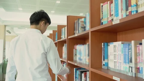 Young asian is walking between book shelf,choose books in the library,Concept Stock Footage 122586214