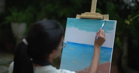 Young asian woman adding final sky layers to seascape using soft brushstrokes Stock Footage 329669744