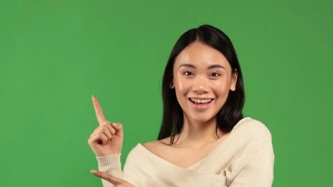 Young asian woman pointing up with hand gesture isolated on green background Stock Photos