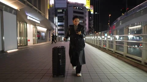 Young Asian woman pulling suitcase and using smartphone on city street walk.. Stock Footage 337945247