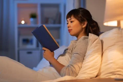 Young asian woman reading book in bed at home Stock Photos