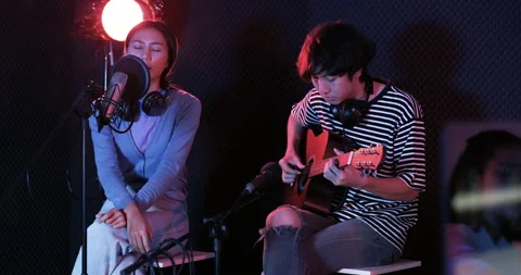 Young asian woman singing while man in background playing acoustic guitar Video stock 138942151