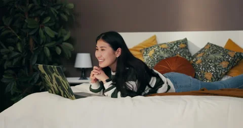 Young Asian woman using computer in bed. Smiling girl makes video call on laptop Video stock 229428705