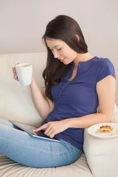 Young asian woman using her tablet pc and holding mug of coffee Stock Photos