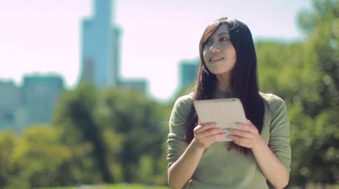 Young Asian Woman using iPad tablet pc computer in a park Stock Footage
