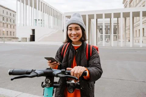 Young asian woman using mobile phone for electric scooter's rent outdoors Stock Photos
