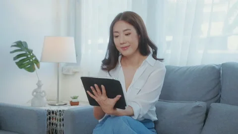 Young asian woman using  tablet on sofa in living room Vidéo 212890589