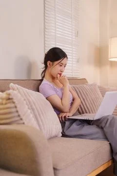 Young Asian women using laptop computer working from home sitting on sofa i.. Foto stock