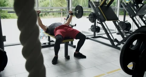 Young athlete is doing bench press in gym.Man lies on bench and does exercise Видео 116513554
