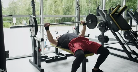 Young athlete is doing bench press in gym.Man lies on bench and does exercise Video stock 116619322