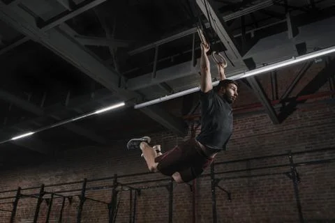 Young athlete doing pull-ups on gymnastic rings at cross fit gym. Handsome ma Fotos de archivo