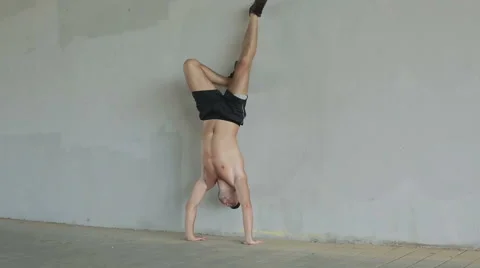 The young athlete is doing pushups on hands standing upside down near the wall. Stock Footage 68757624