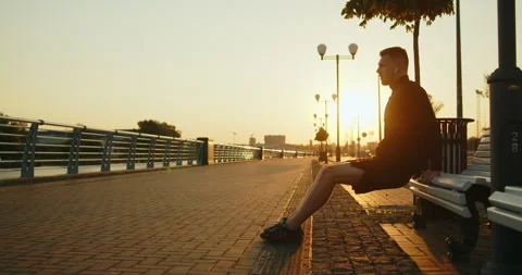 Young athlete doing reverse push-ups from a bench on a city street at sunset Stock Footage 276544309