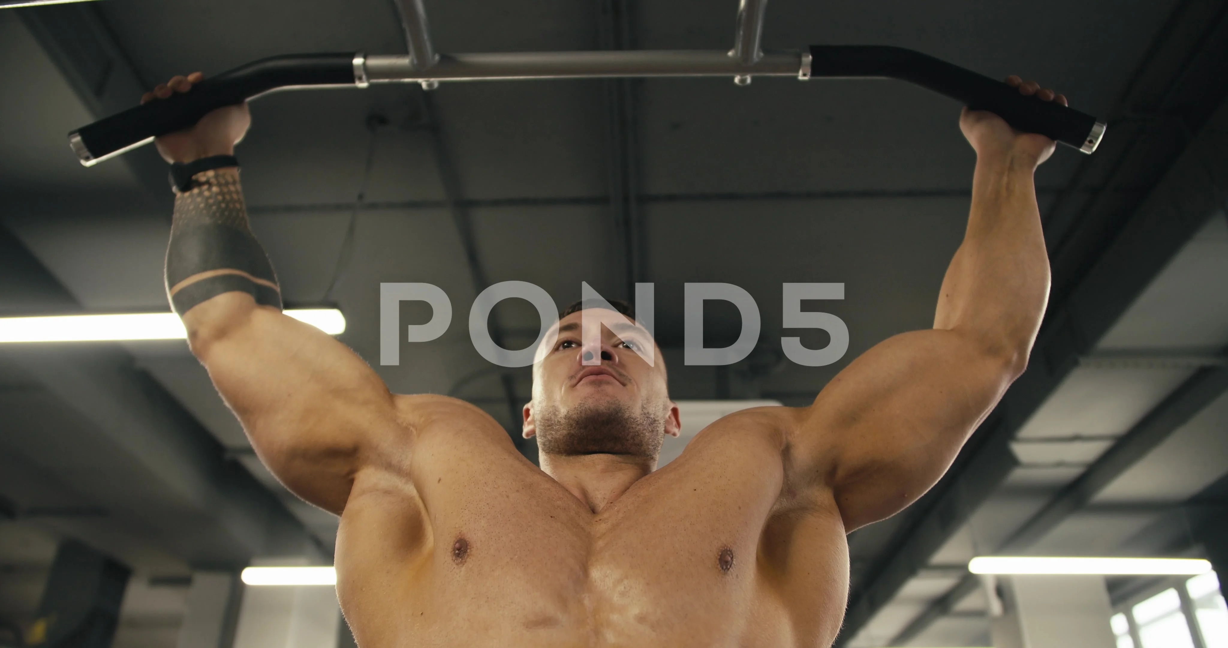 A young athlete with a naked torso performs pull-ups in the gym on a special