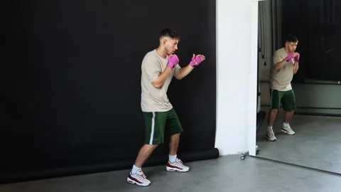 Young athlete practices boxing techniques in a training studio with a mirror Stock Footage 312383816