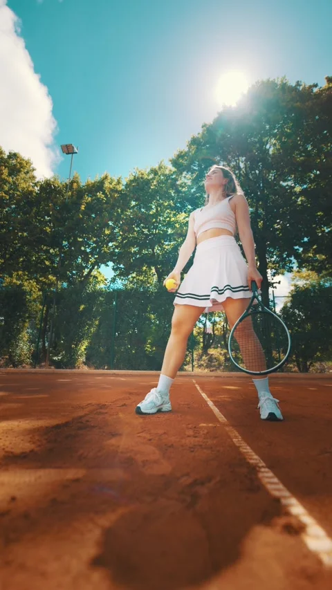 Young athlete prepares to serve on a clay tennis court during sunny afternoon Stock Footage 338243353