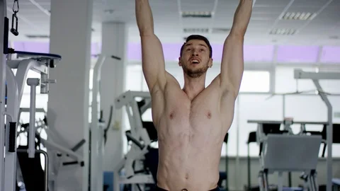 Young athlete pulls up his legs on a crossbar in a gym Vídeos de archivo 105945275