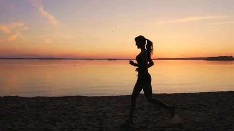 Young athlete runner is runing along the shore of the lake at sunset Stock Footage 77696236