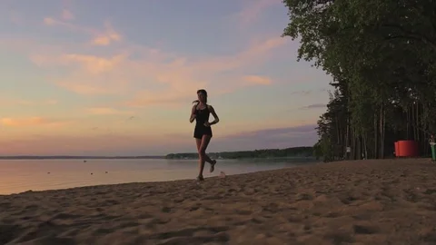 Young athlete runner is runing along the shore of the lake at sunset Stock Footage 77696375