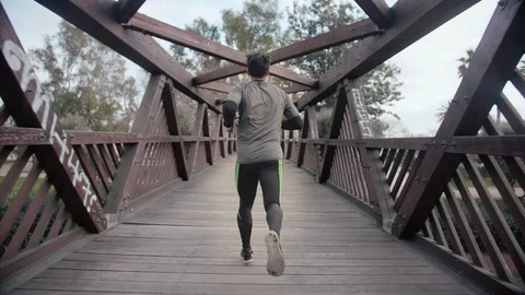 Young athlete running away from the camera through an urban wooden bridge Stock Footage 104489645